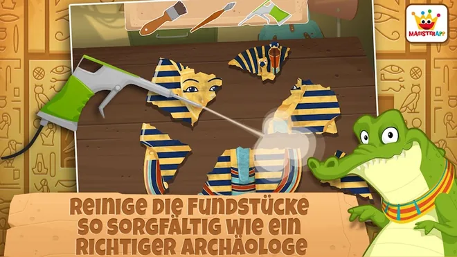Archäologe: Altes Ägypten 2-5: blau-goldene Maskenbruchstücke auf einer Holzplatte werden mit einem Druckreiniger abgespritzt, oben liegen zwei Pinsel bereit